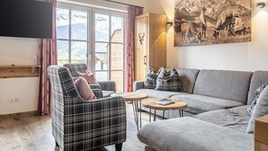 A modern living room with a sofa, armchair, and coffee table. A large window offers a view of mountains.