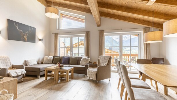 Un amplio salón con techo de madera, ventanas grandes, un conjunto de sofás, una mesa de comedor con sillas y una mesa de centro de madera.
