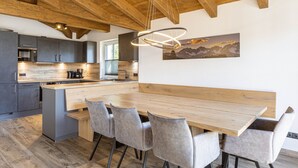 Une cuisine moderne avec des poutres en bois, un îlot central, des meubles de couleur grise et un coin repas comprenant une table en bois et des chaises grises.