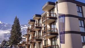 Ein mehrstöckiges Hotel mit Balkonen und Blick auf die Berge, mit einem Schild, das 'Alps Resorts' anwirbt.