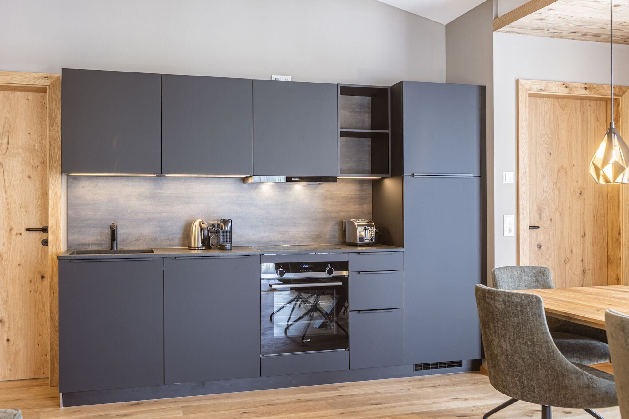 Eine moderne Küche mit grauen Schränken, einem eingebauten Backofen und einem Holzespeisetisch mit grauen Stühlen.