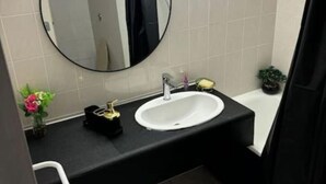 A bathroom with a round mirror, a white sink, a black countertop, and a small potted plant. - La belle étape and Parking  (Carquefou)