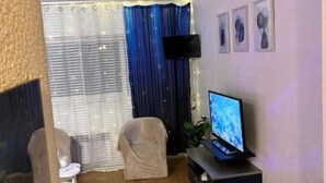 Un salon moderne avec un téléviseur à écran plat, un canapé, un fauteuil et une fenêtre avec des rideaux.