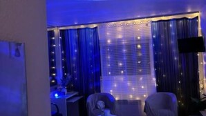 Une pièce avec un projecteur au plafond, un bureau avec un ordinateur, une chaise et une petite table avec une lampe.