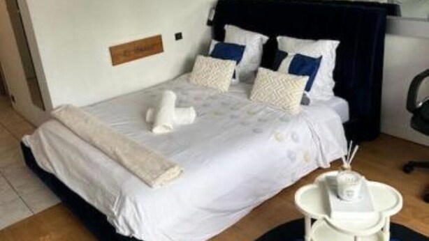 Un lit bien fait, avec une tête de lit sombre, une petite table de chevet avec une lampe et une plaque nominative accrochée au mur.
