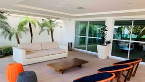 Uma área de estar moderna ao ar livre, com sofá, mesa de centro de madeira e cadeiras laranja e azuis.