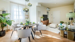 Un salon moderne avec un coin repas, comprenant une table ronde, des chaises grises, un canapé et un téléviseur.