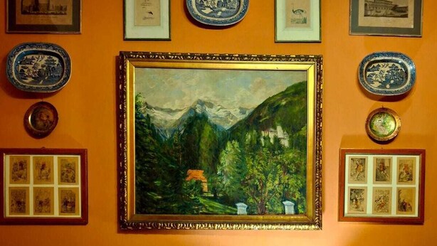 Une pièce comprenant un tableau de paysage encadré, une table avec une lampe et divers tableaux encadrés accrochés au mur.