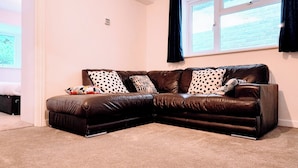 A brown leather sectional sofa with patterned cushions, a small table, and a window with curtains.