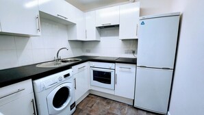 A compact kitchen with white cabinets, a washing machine, a built-in oven, and a refrigerator.