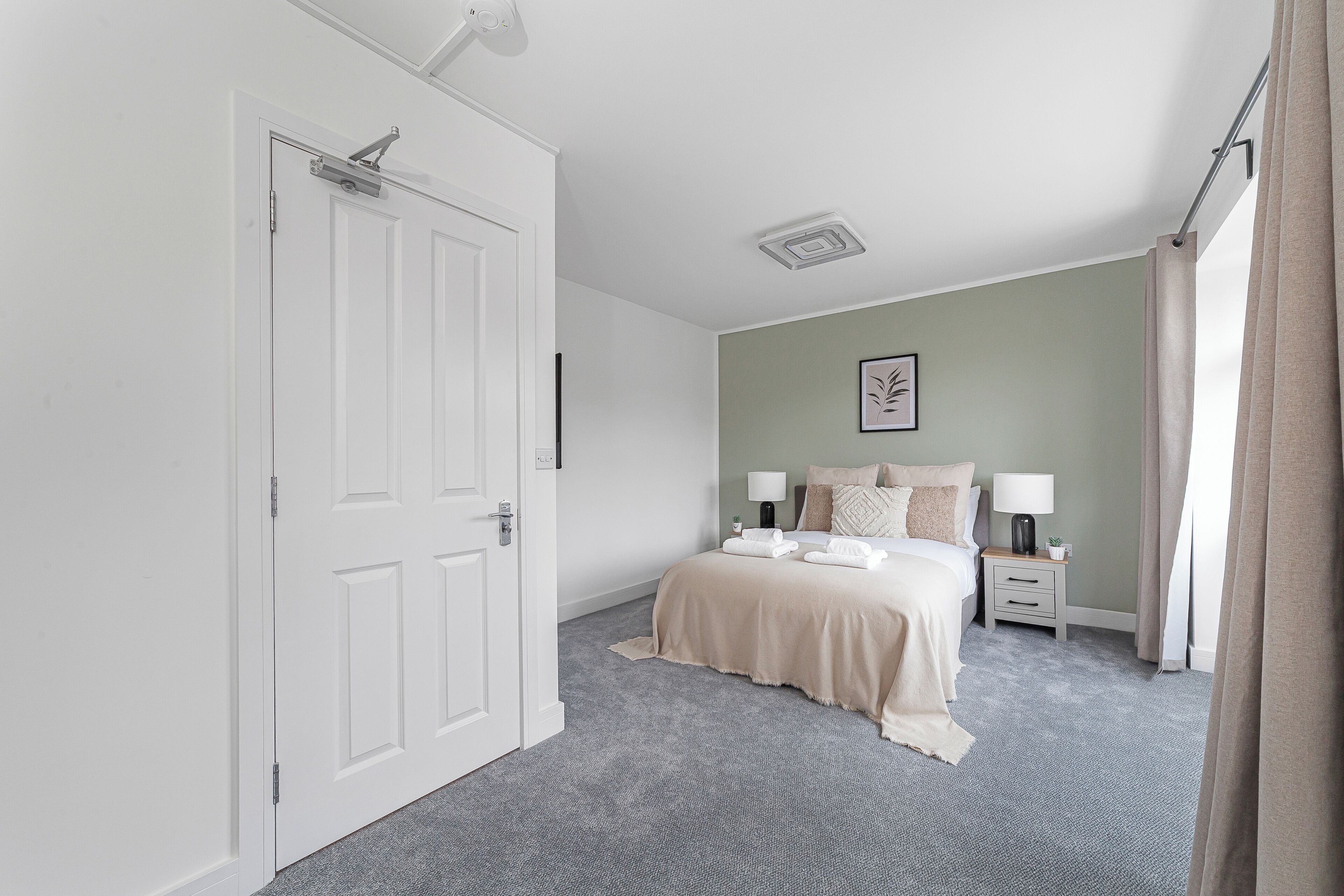 A bedroom with a bed, bedside tables, a nightstand, a lamp, and a window with curtains.