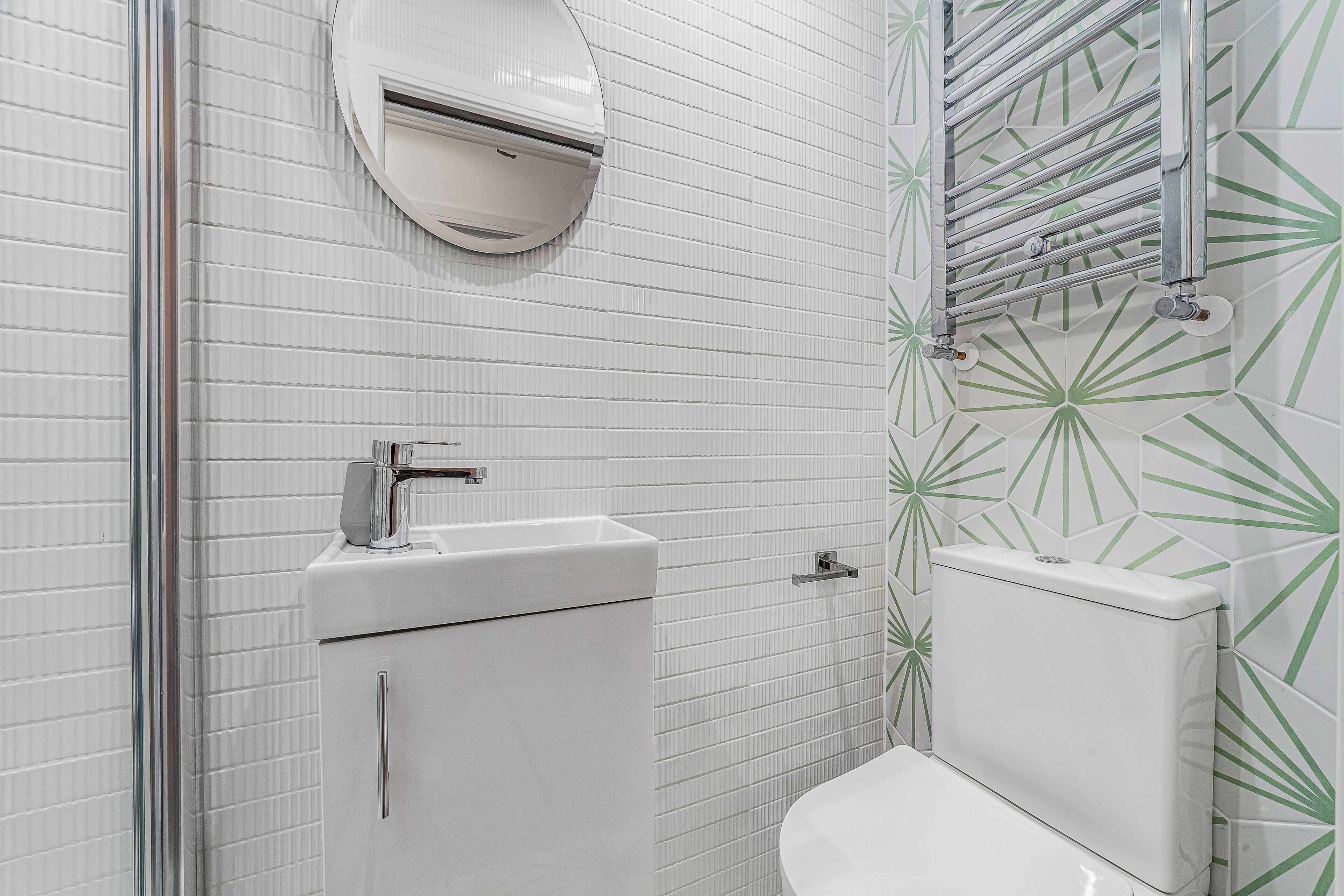 Un baño con paredes de azulejos blancos, un inodoro, un lavamanos y un perchero para toallas.