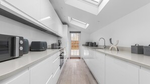 A modern kitchen with white cabinetry, a skylight, a built-in oven, and a coffee station. - Spacious Room In Morden (Morden)