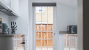 A modern kitchen with a skylight, white cabinets, and a view of a wooden fence outside. - Spacious Room In Morden (Morden)
