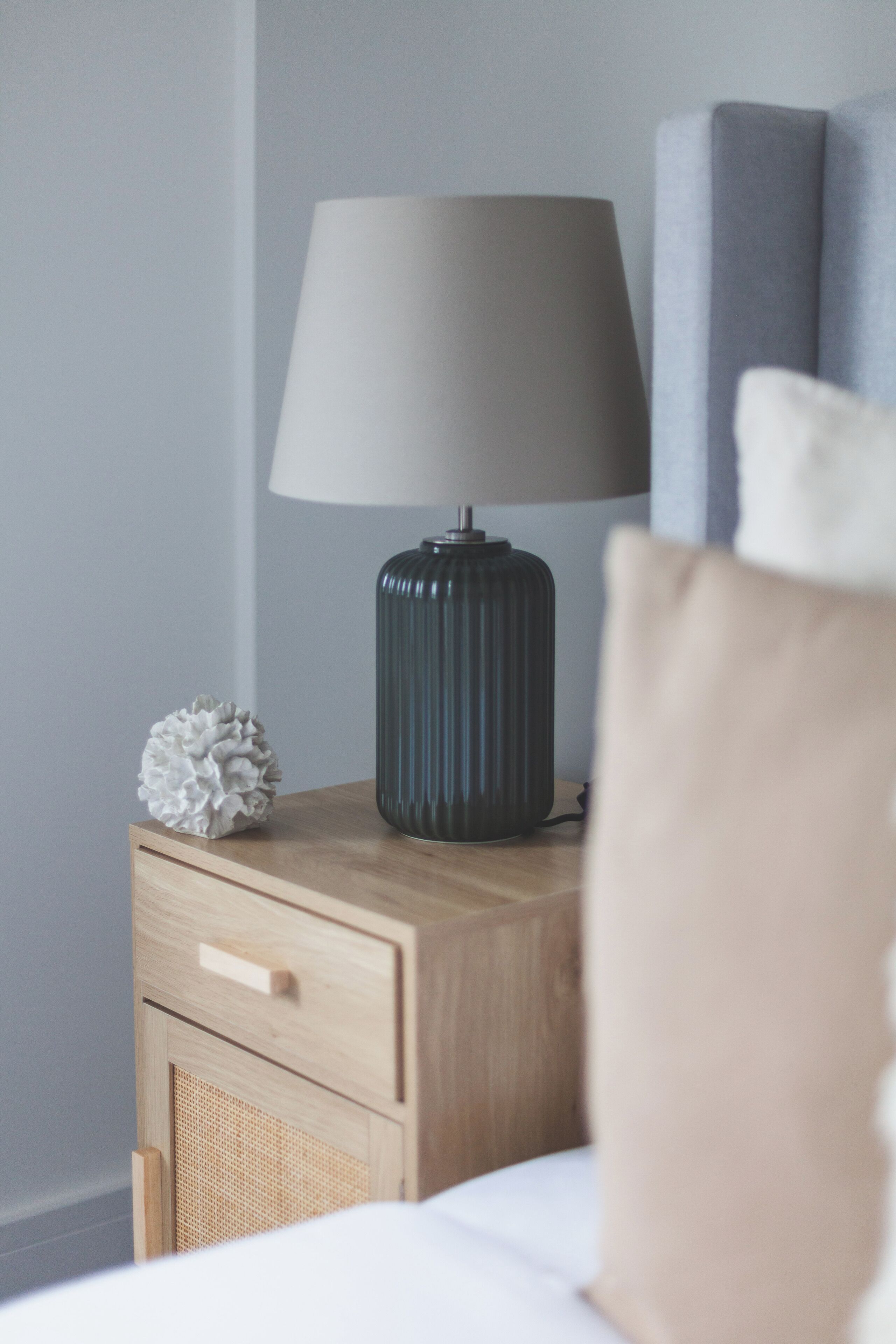 A bedside table with a lamp, a decorative object, and a pillow.