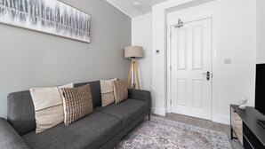 A modern living room with a grey sofa, patterned cushions, a floor lamp, and a large abstract painting on the wall. - Spacious Room In Morden (Morden)
