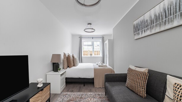 A modern hotel room with a large bed, a flat-screen TV, a sofa, and a painting on the wall. - Spacious Room In Morden (Morden)
