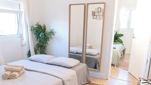 A hotel room with two beds, a large mirror, a potted plant, and a wooden floor.