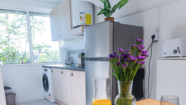 A modern kitchen with a washing machine, a refrigerator, and a dining area with a table set for breakfast.