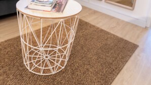 A modern living room with a grey sofa, a round coffee table with a geometric design, a brown rug, and a large mirror reflecting the room.