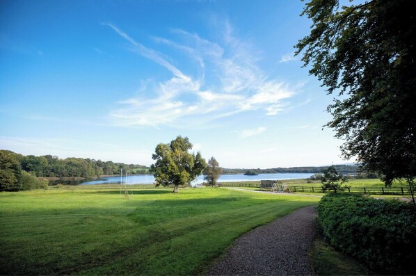 A grassy field with a path leading to a lake, surrounded by trees and a fence. - Luxury and elegant lakeside lodges, Boating activities and pet friendly.
(Sixmilebridge)