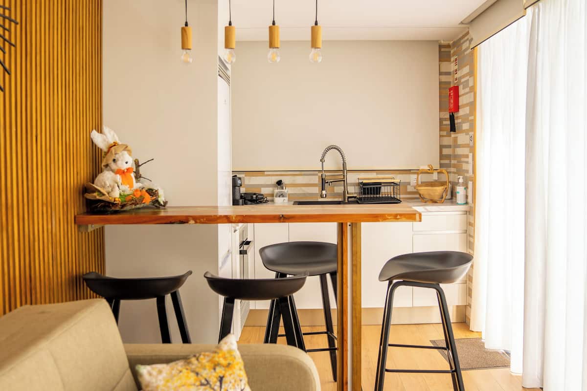 A modern kitchen with a wooden countertop, black bar stools, and pendant lighting.
