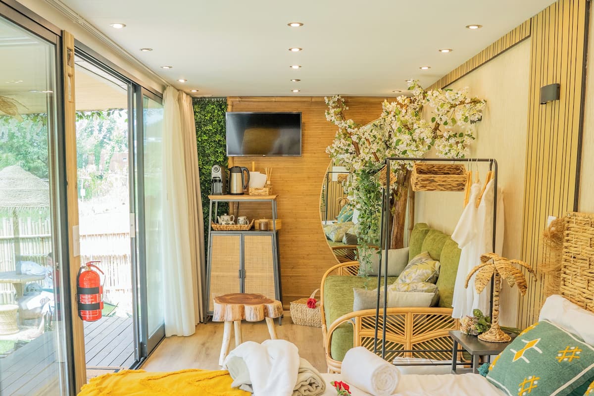 A modern bedroom with a large bed, a TV mounted on the wall, and a balcony with a fire extinguisher.