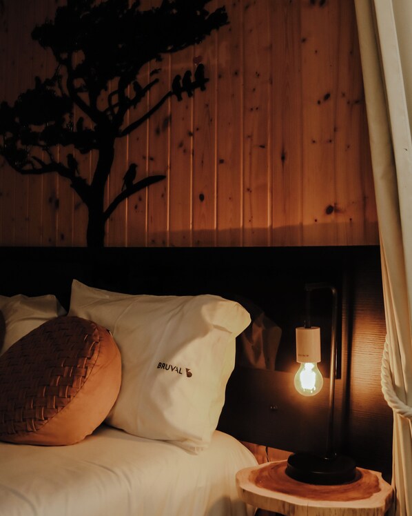 A wooden-paneled room with a bed, pillows, and a nightstand with a lamp.