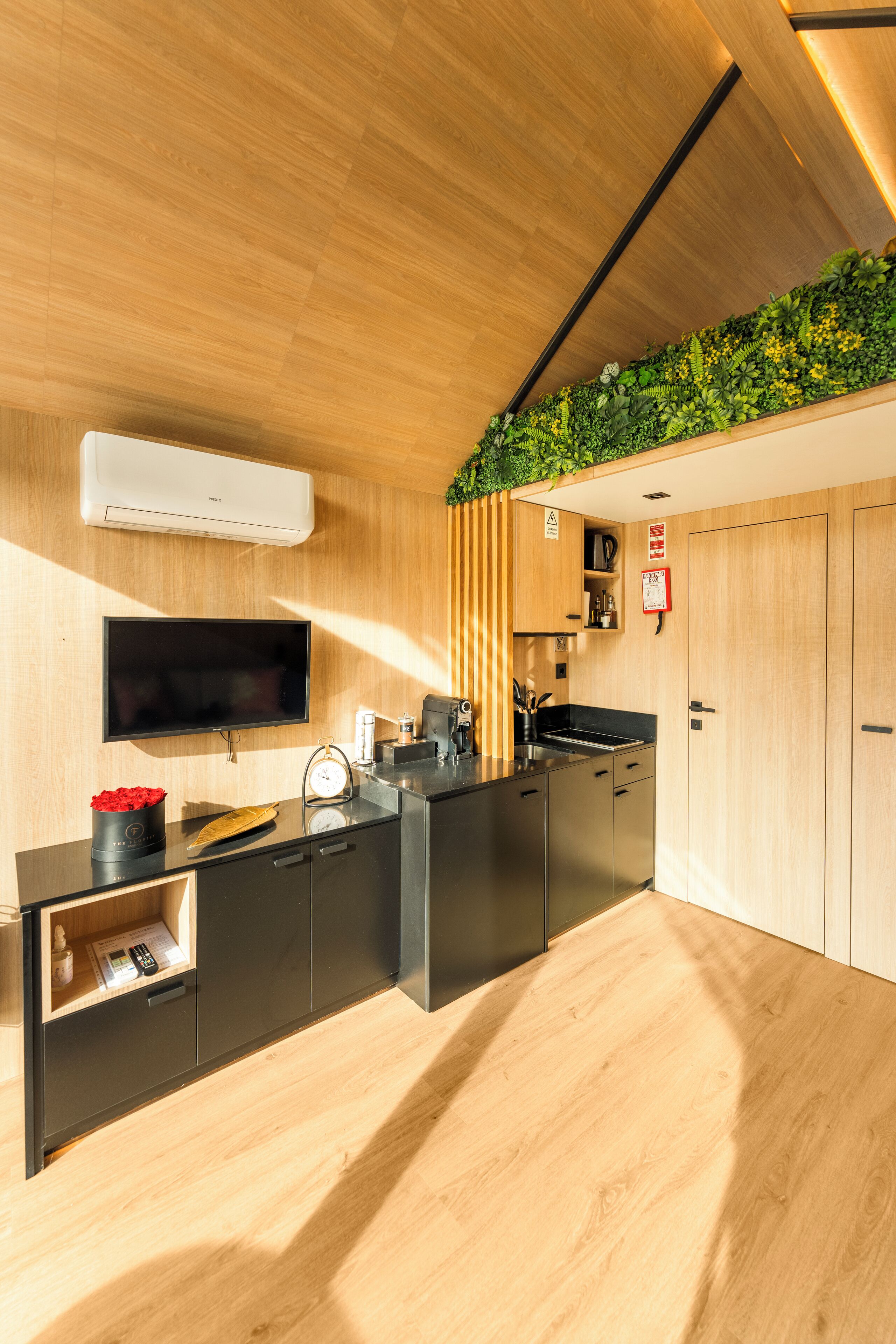 A modern kitchen with wooden cabinetry, a black countertop, a built-in herb garden, a flat-screen TV, and a coffee machine.