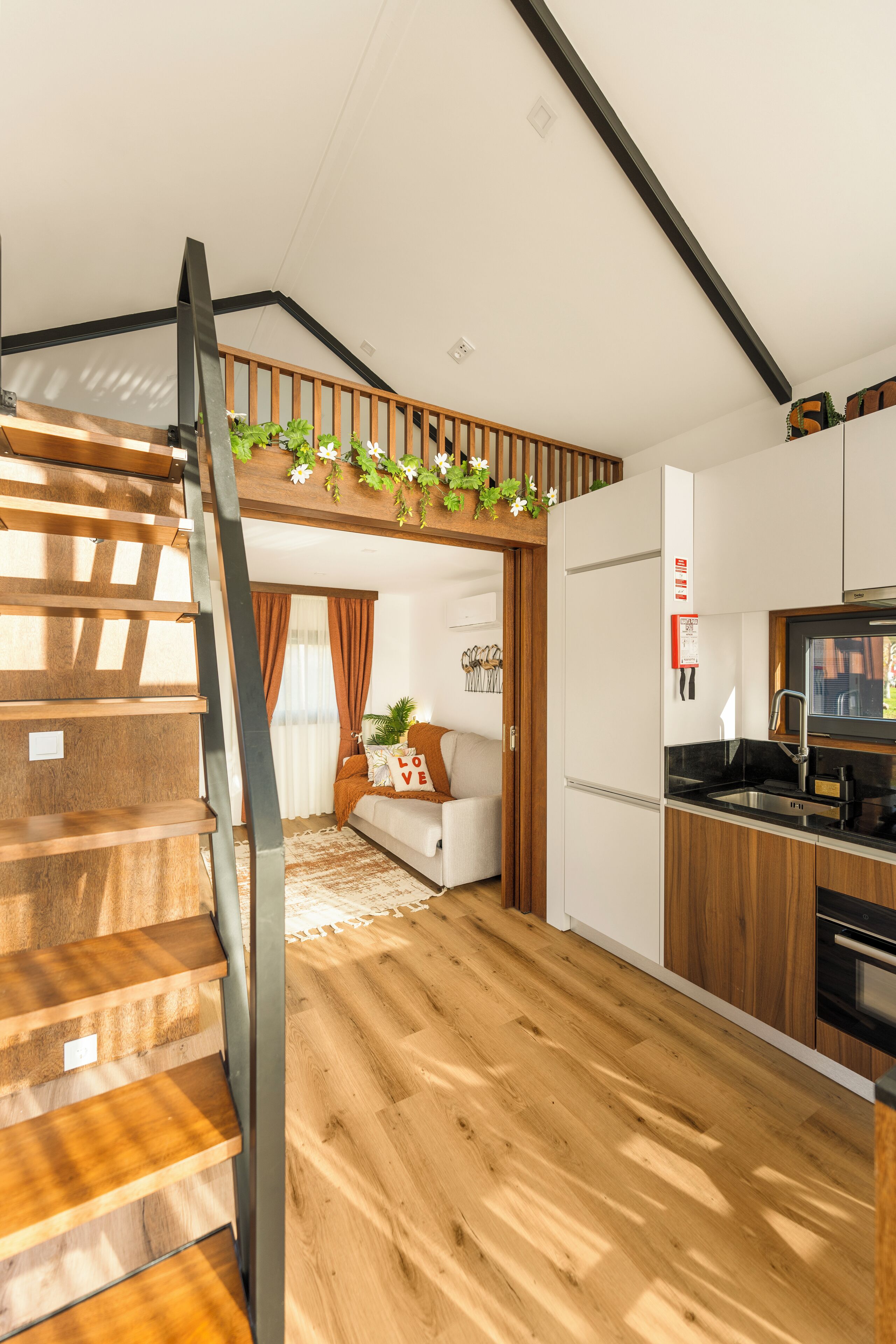 A modern kitchen with wooden flooring, a built-in oven, and a stainless steel sink.