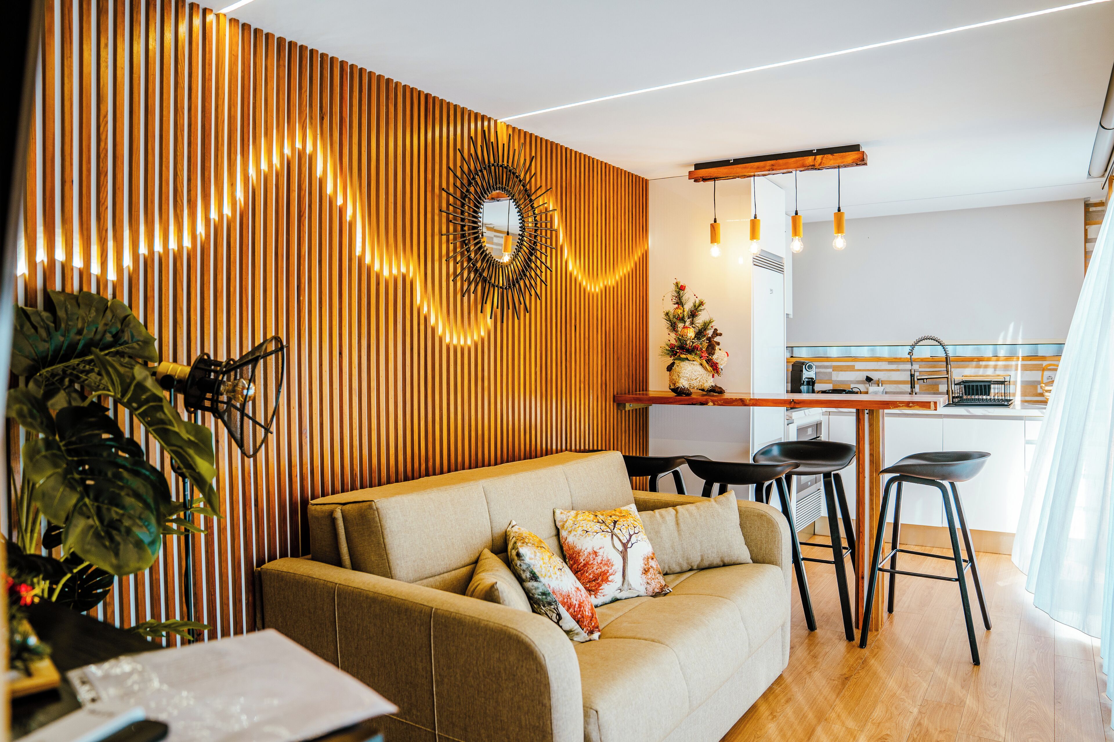 A modern living room with a sofa, a dining area with stools, and a kitchen in the background.