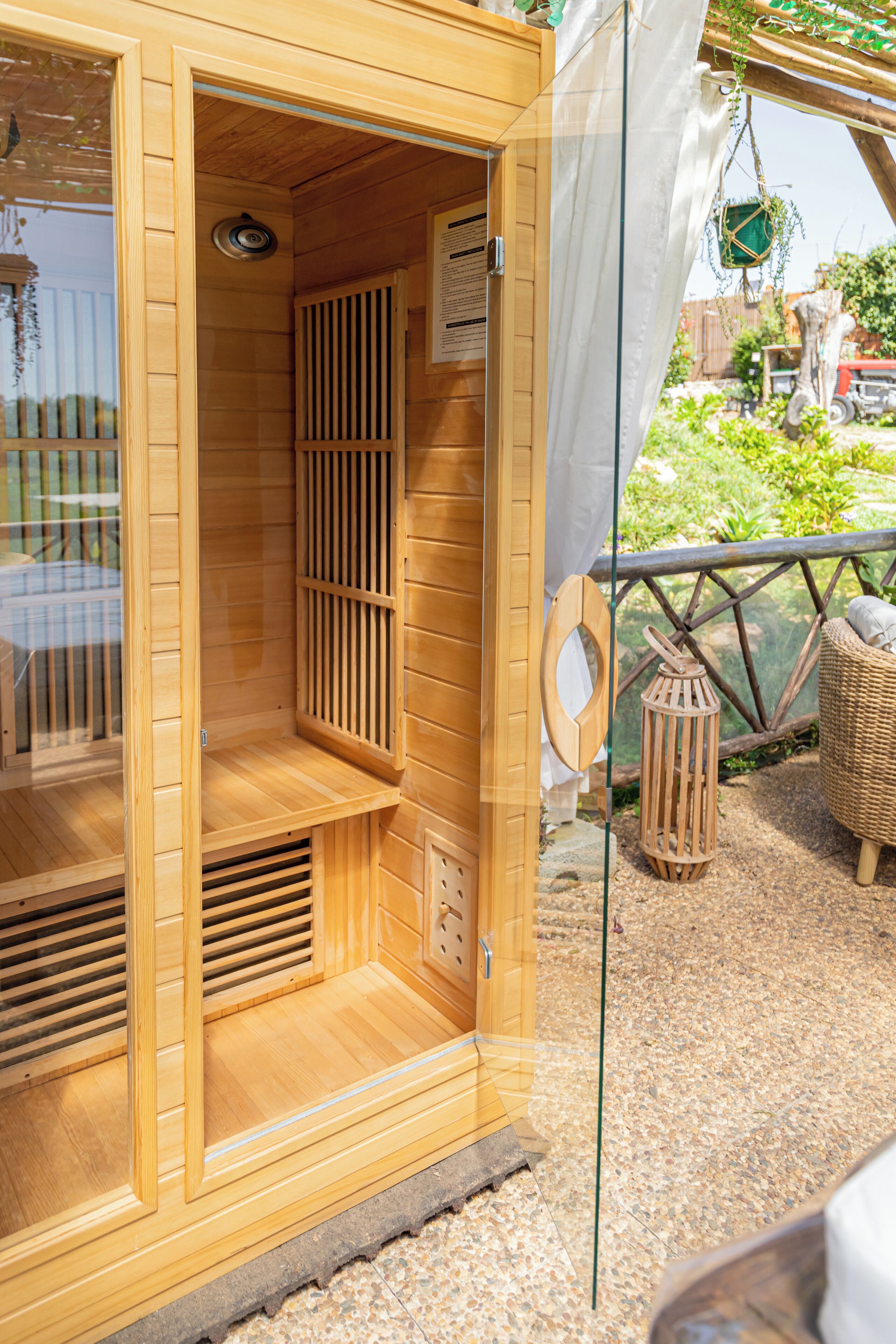 A wooden sauna with a glass door, a ventilation system, and a wicker chair outside.