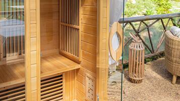 A wooden sauna with a glass door, a ventilation system, and a wicker chair outside.