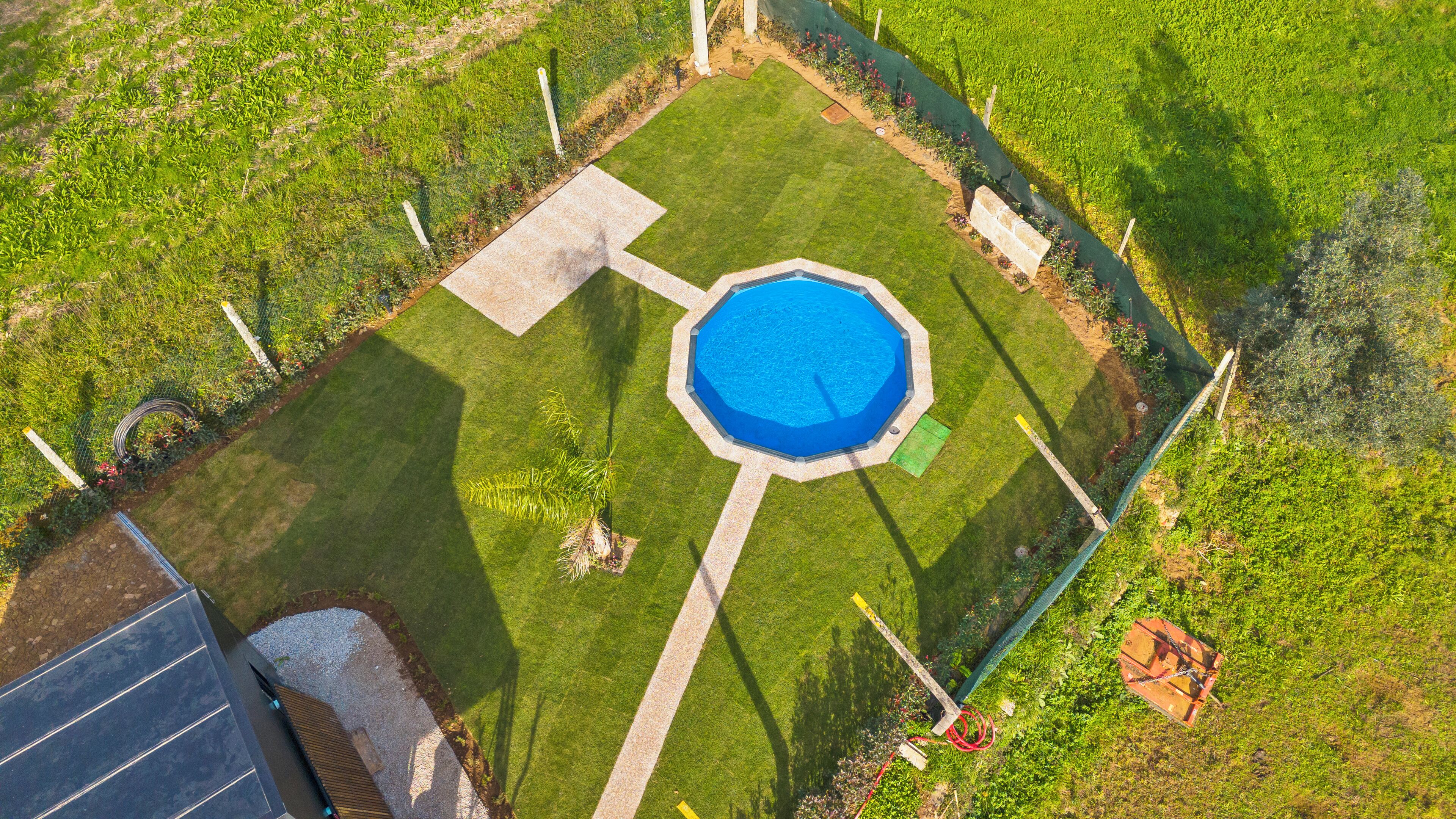 An octagonal swimming pool surrounded by a well-maintained lawn, with a concrete deck and a small garden area.