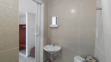 Un baño con baldosas color crema, un lavamanos blanco, un inodoro y un espejo.