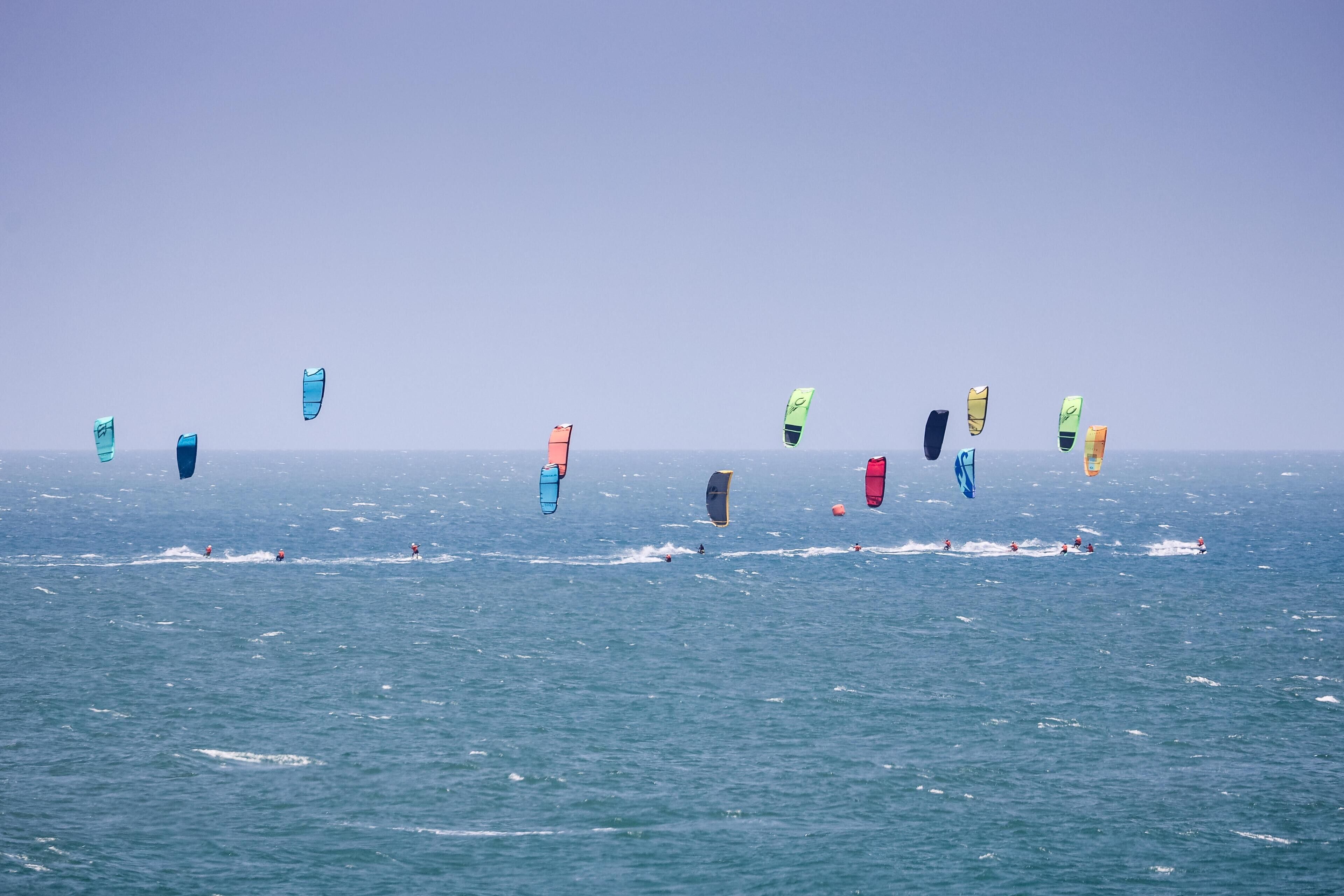 A view of the ocean with multiple kites in the sky.