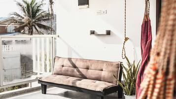 A balcony with a cushioned sofa, a hanging chair, and a potted plant.