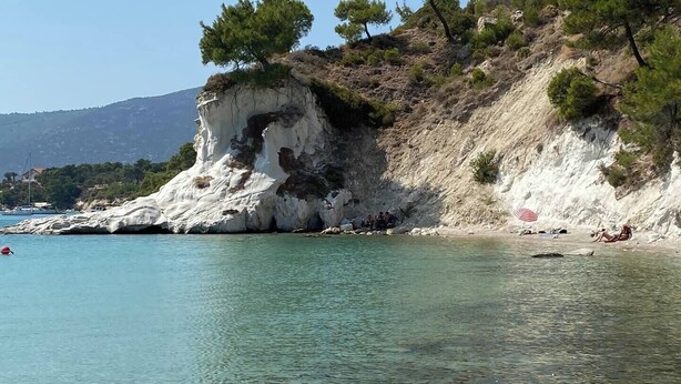 A coastal area with clear water, rocky cliffs, and sparse vegetation.