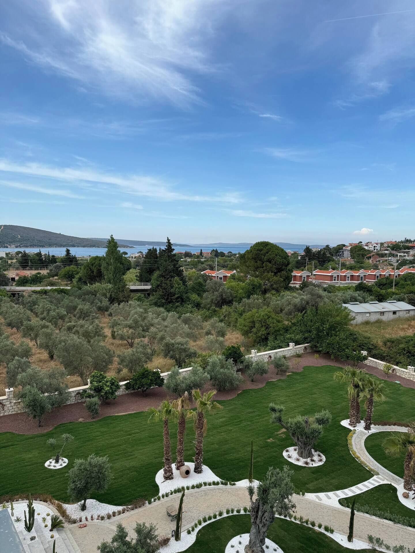 Ein angelegter Garten mit Wegen, Palmen und Blick auf eine Küstenstadt.