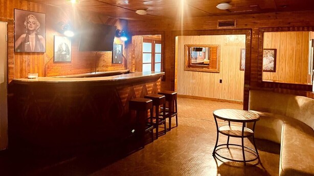 A bar area with wooden walls, a bar counter, stools, and framed pictures on the wall. - Central 3-bedroom house in Redding with Pool & Vintage Bar Room (Redding)