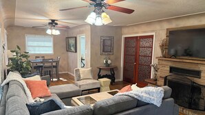 A living room with a sofa, armchairs, a coffee table, a fireplace, a TV, and ceiling fans. - Central 3-bedroom house in Redding with Pool & Vintage Bar Room (Redding)