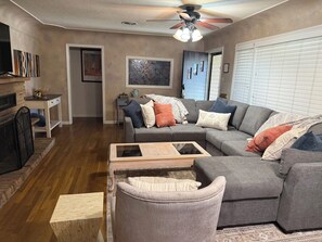 A living room with a gray sectional sofa, a wooden coffee table, a fireplace, and a ceiling fan.