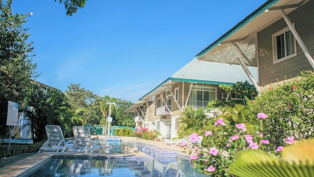Un espace piscine avec des chaises longues, un bâtiment doté d’un balcon et une végétation luxuriante.