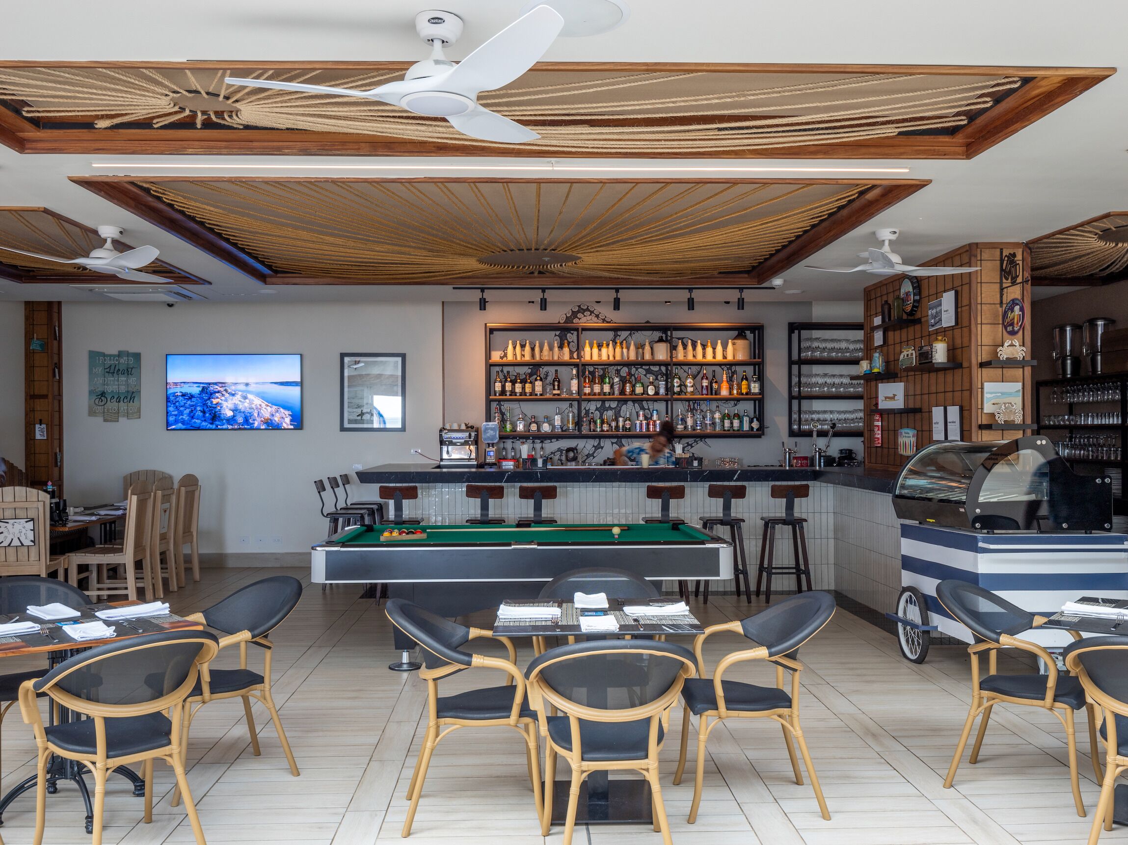 Eine Barbereich mit Billardtisch, Barhocker und Grillstation.