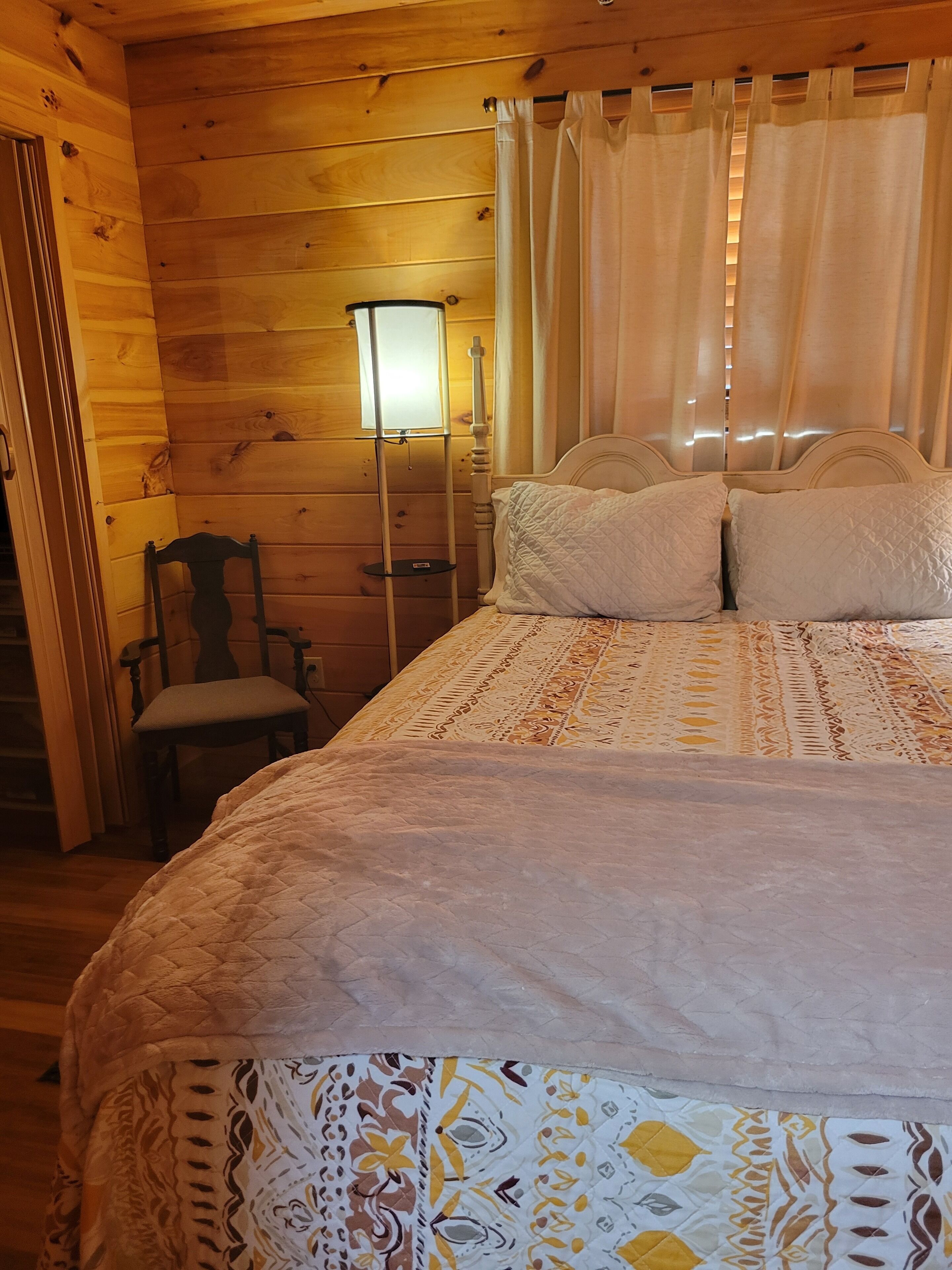 Una habitación tipo cabaña de madera con cama, una silla y una lámpara de pie.