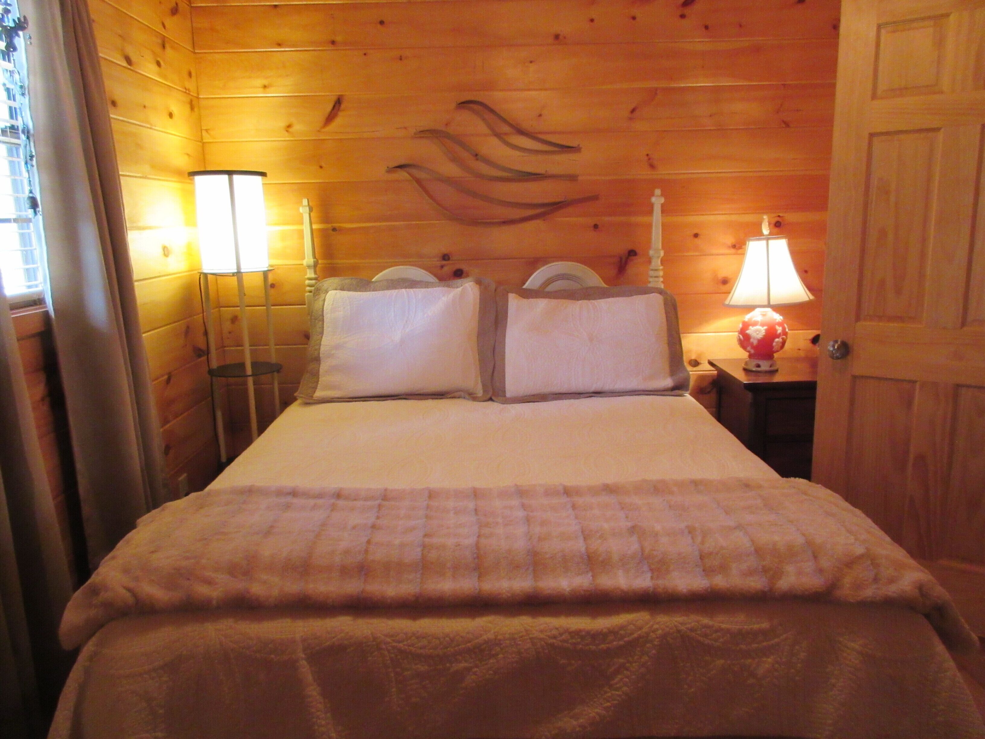 A wooden room with a bed, two bedside lamps, and a door.