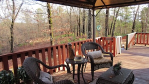 Une terrasse couverte, dotée de meubles en osier et offrant une vue sur une forêt.