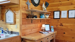 L’intérieur d’un chalet en bois comprend un coin cuisine, des étagères en bois ornées d’objets décoratifs, une horloge murale et des certificats encadrés.