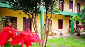 A building with numbered doors, a hammock, and a garden with a tree and red flowers.