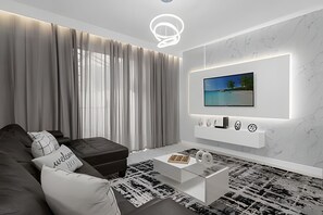 Ein modernes Wohnzimmer mit einer Couch, einem Hocker und einem Couchtisch. Ein Fernseher ist an der Wand montiert, darunter befinden sich dekorative Elemente.